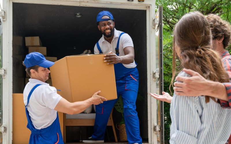 What defines long-distance movers? Two company movers taking box out of truck in front of clients